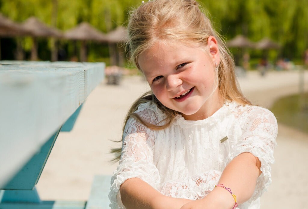 Blije communicant zit op een houten bank tijdens haar communiefeest bij Beachclub Degreez.