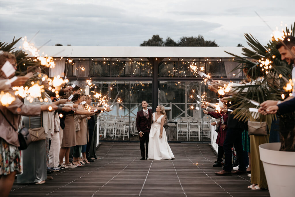 Bruidspaar loopt tussen gasten met sterretjes tijdens een avondbruiloft bij Beachclub Degreez in Limburg.