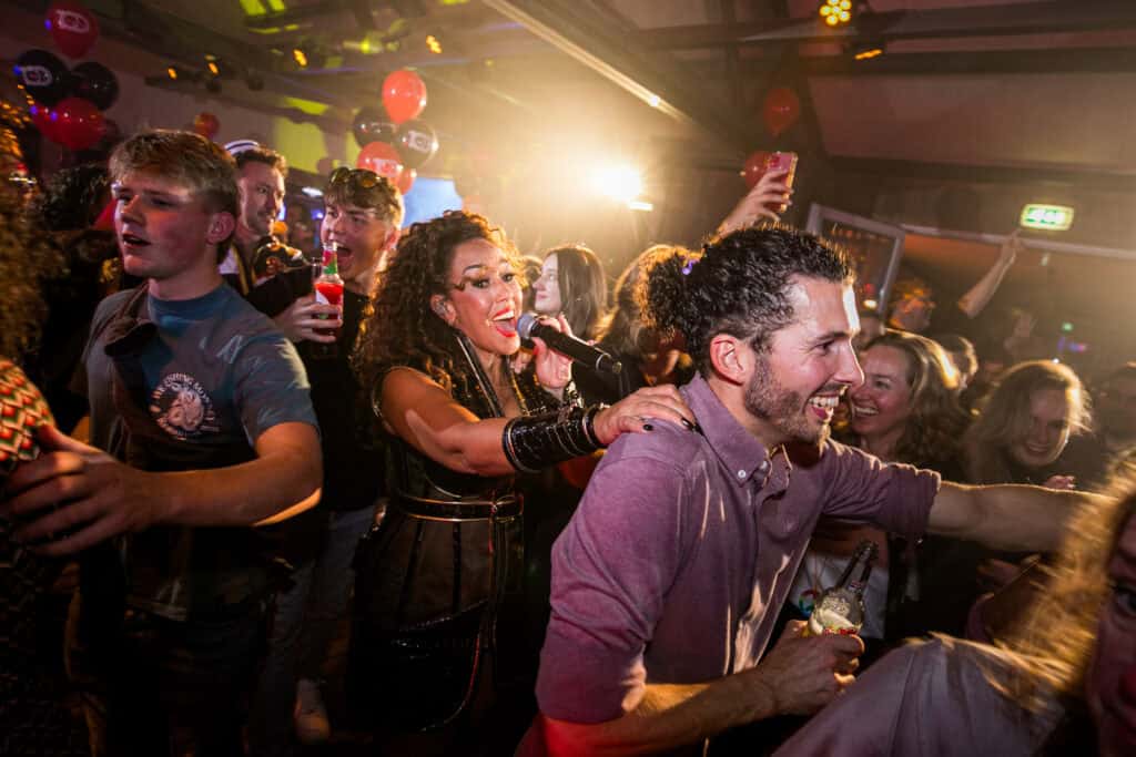 Mensen feesten samen tijdens live entertainment bij Beachclub Degreez, met een zangeres tussen het publiek.