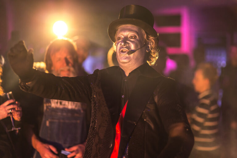 Entertainer met hoed en microfoon treedt op tijdens een bedrijsjubileum bij Beachclub Degreez.