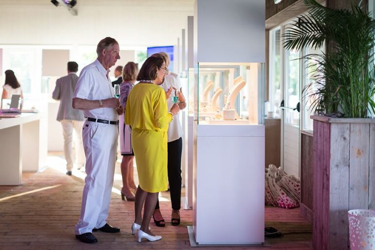 Gasten bekijken sieraden in een vitrine tijdens een exclusieve presentatie bij Beachclub Degreez in Limburg.