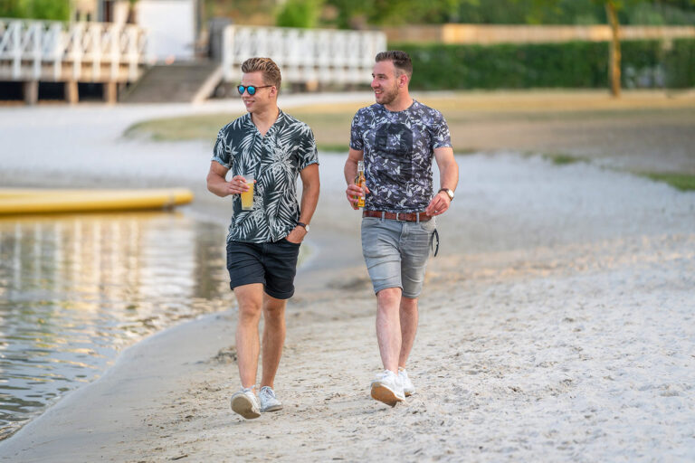 Collega's wandelen met een drankje langs het strand tijdens een personeelsfeest bij Beachclub Degreez.