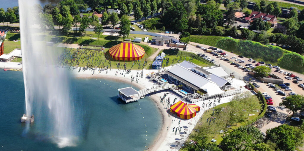 Luchtfoto van Beachclub Degreez aan het water met strand, paviljoen en buitenterrein tijdens een grootschalig evenement.