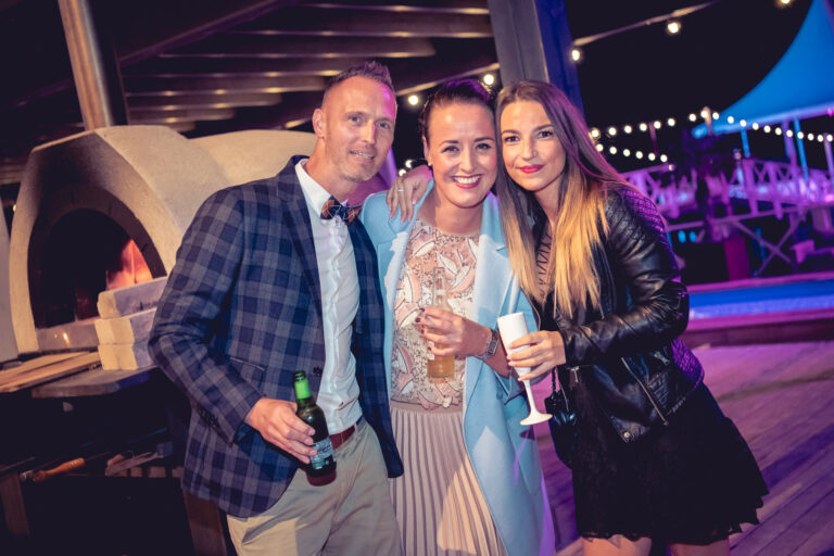 Drie gasten genieten van een winters jubileum bij Beachclub Degreez in Limburg, met sfeervolle verlichting en vuur op de achtergrond.