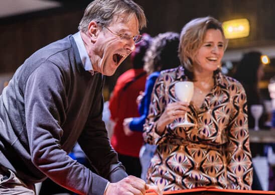 Collega’s lachen en juichen tijdens het spelen van Airhockey, onderdeel van de teambuildingactiviteit Battle to the Top van Group Events bij Beachclub Degreez in Limburg.