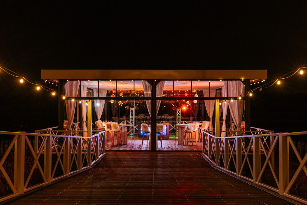 Verlicht waterpaviljoen bij Beachclub Degreez in Panheel tijdens een quizavond, met sfeervolle verlichting en een uitzicht over het water