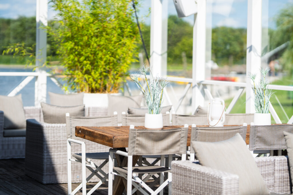 Sfeervol terras aan het water bij Beachclub Degreez met houten tafels, comfortabele zitplaatsen en uitzicht over het meer.